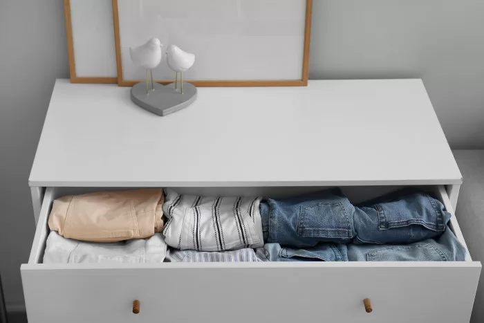 Cômoda com roupas na gaveta e decoração na parte superior.
