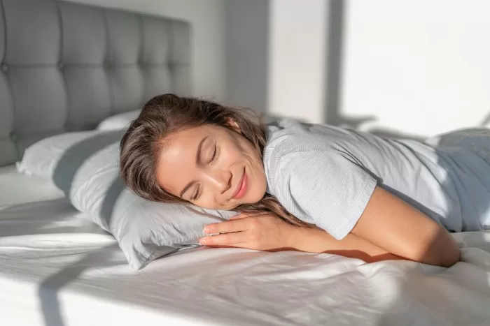 Mulher abrindo cortinas ao acordar pela manhã.