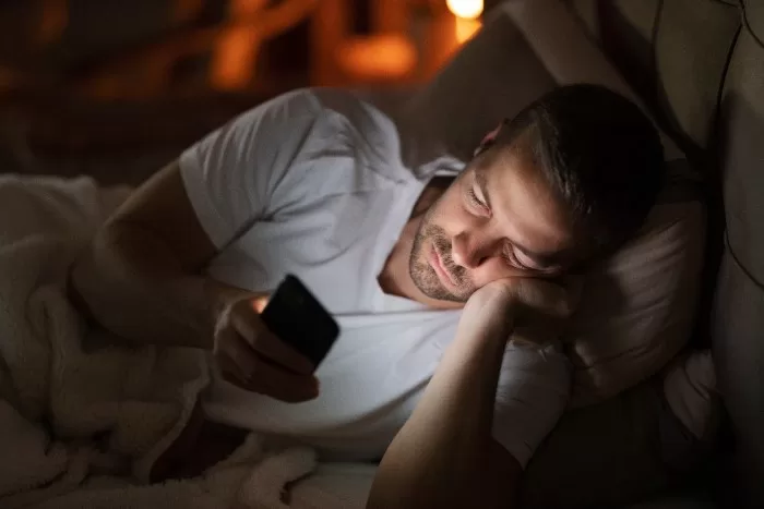 Pessoa mexendo no celular sem conseguir dormir.