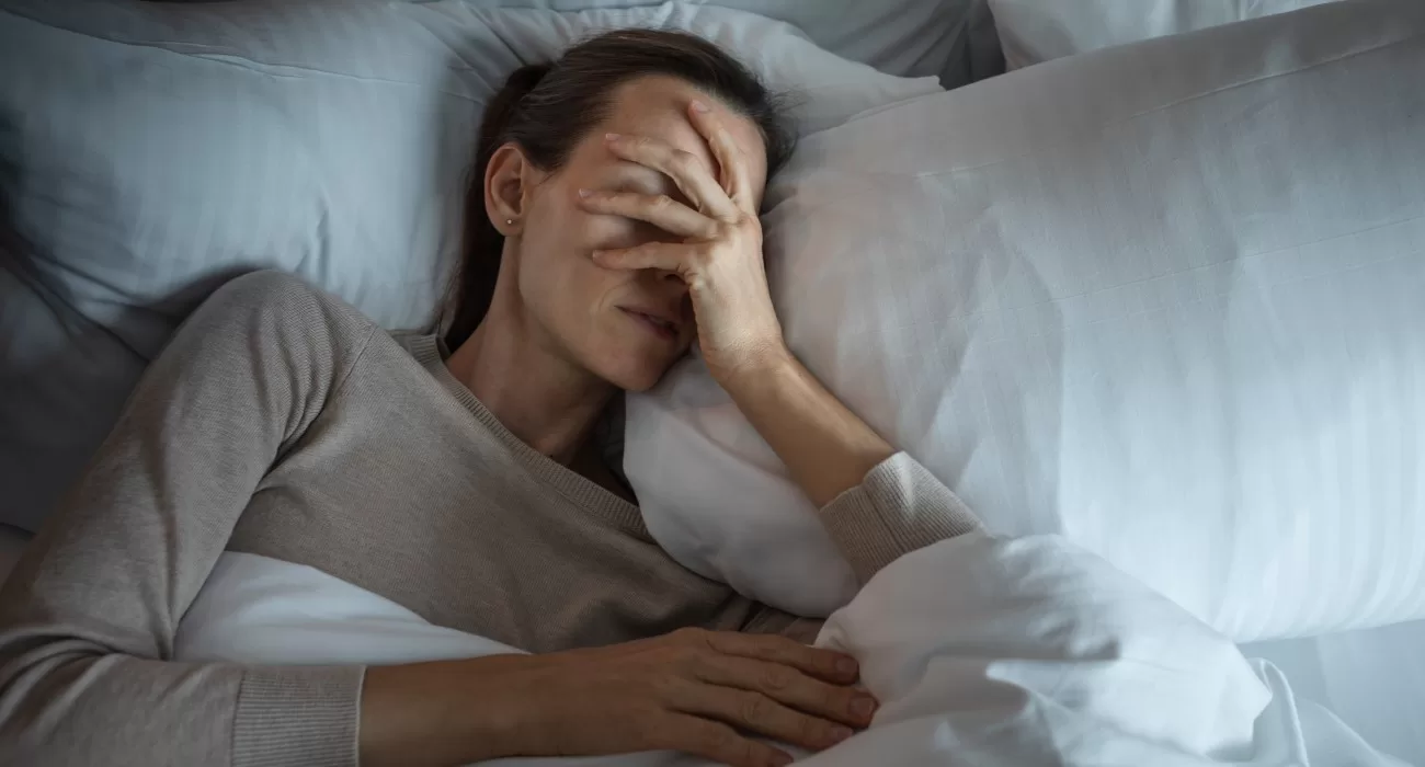 Mulher com mão no rosto sem conseguir dormir.