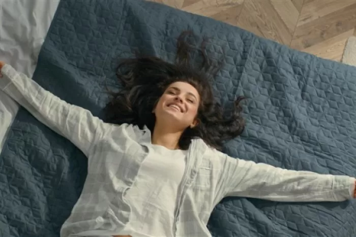 Mulher deitada de braços abertos em uma cama e sorrindo