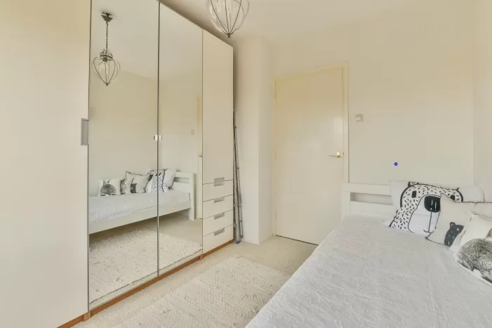 Um quarto na cor bege com portas de armário espelhadas