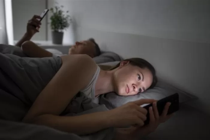 Casal deitado em uma cama mexendo no celular