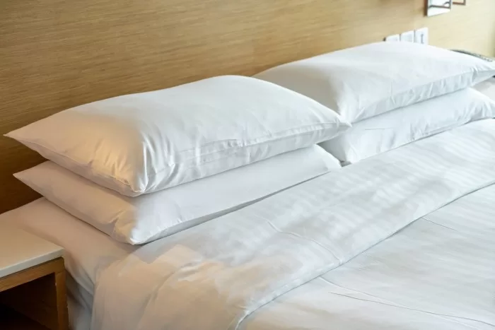 Uma cama com lençol e travesseiros brancos.