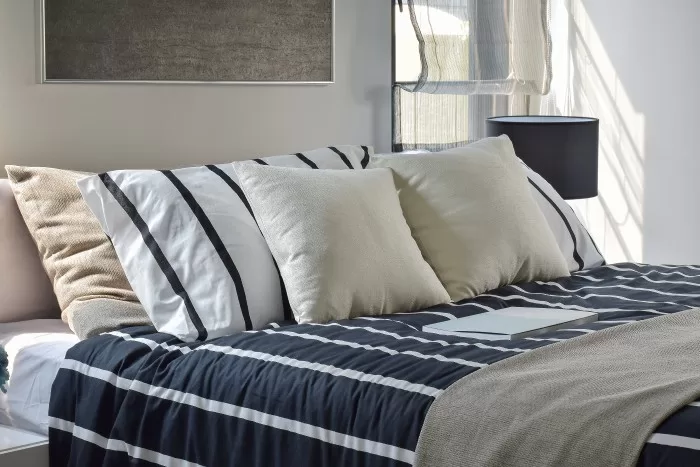 Cama com lençol acolhedor listrado azul e branco e travesseiros em cima.