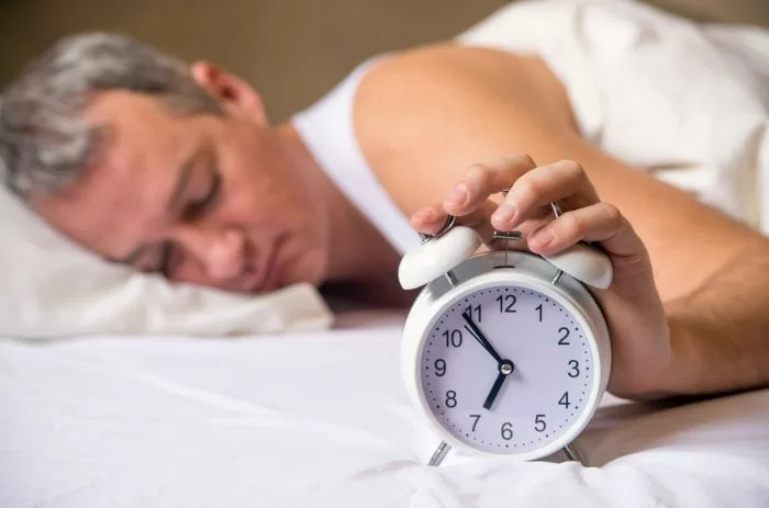 Homem desligando despertador após uma noite de sono.