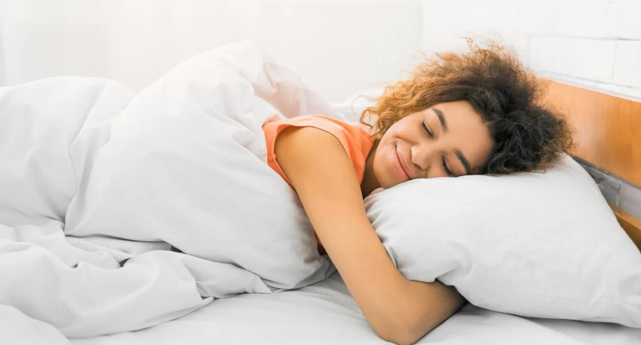 Mulher deitada dormindo e abraçada ao travesseiro.