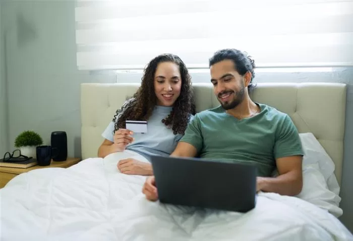 Casal feliz na cama com notebook no colo