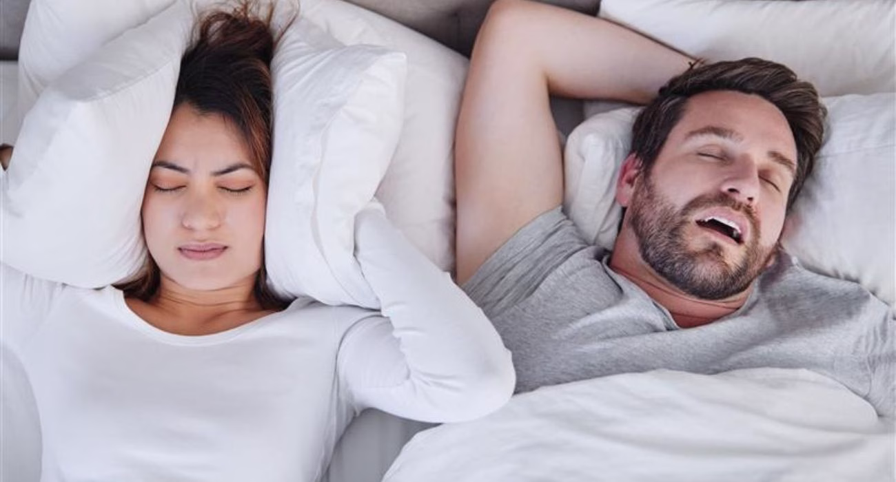 Casal na cama. Homem dormindo e mulher tampando o ouvido.